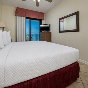 Brightly decorated master bedroom featuring a king bed, a flat-screen TV, and access to a balcony with a view of the beach