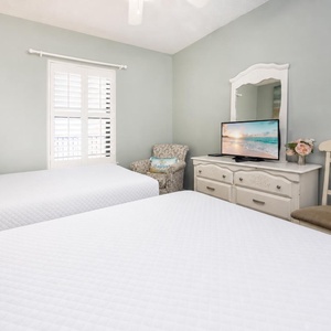 Enjoy restful nights in this inviting guest bedroom with two double beds, a TV, and a cozy chair for relaxation