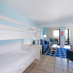 Living area featuring a twin bunk bed, a blue sofa with colorful pillows, and sliding doors leading to a beachfront balcony