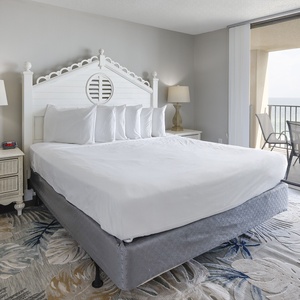 Master bedroom featuring a king bed, stylish nightstands, and a sliding door leading to a spacious balcony