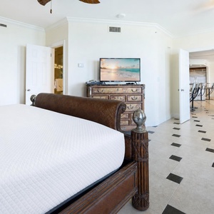 Master suite with a plush king bed, stylish decor, and a view of the spacious living, dining, kitchen, and bar area