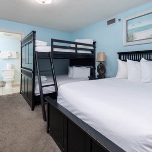 This guest bedroom features a cozy double bunk bed and a queen bed, complemented by soft blue walls and beach artwork