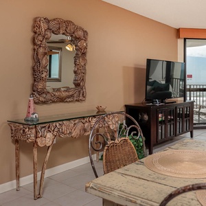 Stylish console table with a decorative mirror and a TV, complemented by a dining area featuring woven chairs and placemats