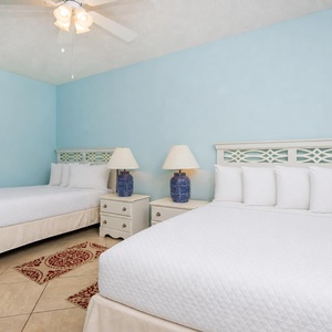 Guest room featuring two double beds, decorative lamps, and a cozy area rug on tiled flooring