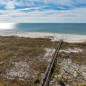 Expansive view of the beach with white sand and gentle waves, framed by lush greenery and a wooden walkway to the shore