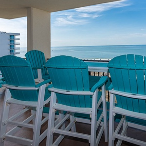 Teal high-top chairs surround a table on the balcony, offering a serene view of the calm beach and gulf waters
