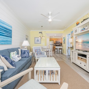 The living area features a blue sofa with decorative pillows and a queen sleeper, a light coffee table, and a large TV