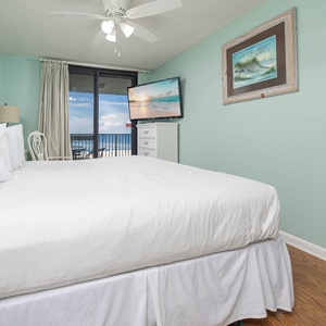 Brightly colored walls frame the master bedroom featuring a plush king bed, a TV, and access to a balcony with a gulf view