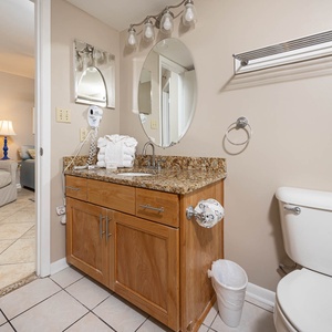 Bathroom featuring a granite countertop with a round mirror, a hairdryer, and a cozy view into the adjacent living area