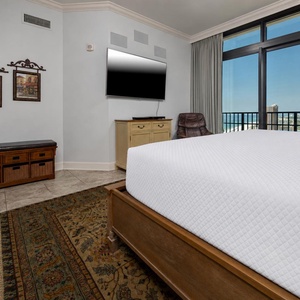 The master bedroom features a cozy king bed, a large TV, and stunning beach views through the balcony door and windows
