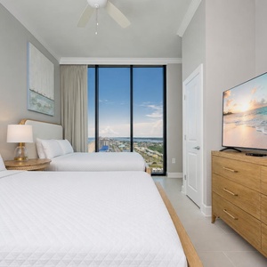 Inviting guest bedroom featuring two comfortable queen beds, a large TV, and stunning beach views