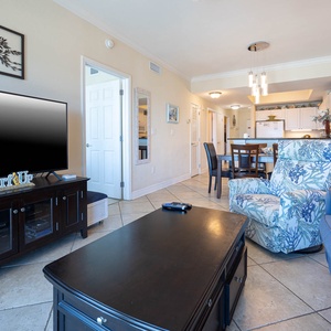 This inviting living area features a large TV, stylish seating, and a view of the bright, open kitchen