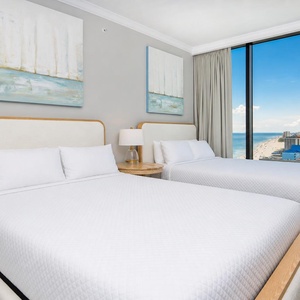 Relaxing guest room featuring two queens, soft lighting, and expansive beach views through large windows