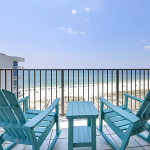 Two bright turquoise chairs and a small table on the balcony offer a perfect spot to enjoy the beach view and relax