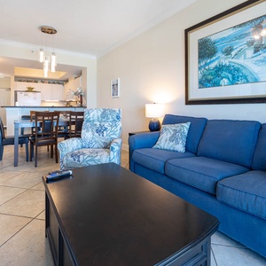 The living area features a cozy blue sofa, a stylish chair, and a dining table, perfect for relaxing and enjoying meals