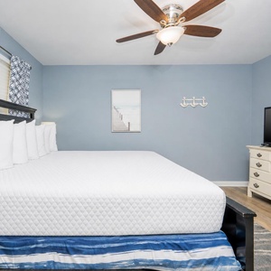 The master bedroom features a large bed with crisp linens, a TV for entertainment, and calming blue walls for a relaxing stay