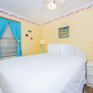 Bright yellow walls frame this guest bedroom featuring a queen bed with white linens, colorful curtains, and cheerful decor