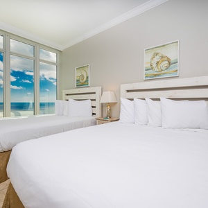 Inviting guest bedroom with two queen beds, large windows framing beautiful views of the beach and stunning sky