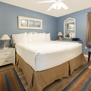 Cozy bedroom featuring a king bed with decorative pillows, a wicker nightstand, and a charming mirror against a blue wall