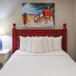 This guest bedroom features a vibrant red bed frame, bright white linens, and a cheerful beach-themed painting