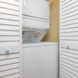 Convenient laundry area featuring a stacked washer and dryer behind sleek white louvered doors for easy access