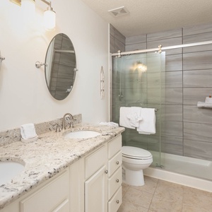 Elegant guest bathroom featuring dual sinks with stylish countertops, round mirrors, and a glass-enclosed walk-in shower