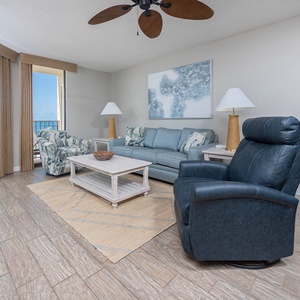 The living room features a blue sofa with a queen sleeper, a comfortable chair, and a view of the beach through large windows
