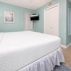 The turquoise walls complement the white bedding in this serene bedroom featuring a mounted TV and natural light