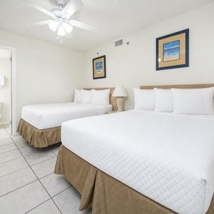 Guest room featuring two double beds, a ceiling fan, and beach-themed artwork, creating a relaxing atmosphere