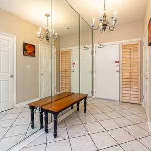 Welcoming entryway features a wooden bench, elegant chandelier, and mirrored wall, creating a bright and airy atmosphere