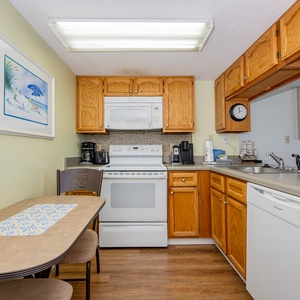 The kitchen features warm wood cabinetry, a dining table for two, and white appliances, perfect for meal prep and relaxation
