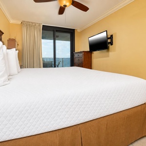 Cozy master bedroom featuring a plush king bed, flat-screen TV, and access to the beachfront balcony