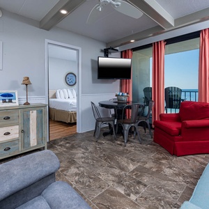 The living area features a couch, cozy red chair, a dining table, with stunning beachfront views through large windows