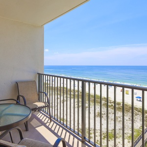 Enjoy a relaxing moment on the balcony with a view of the beach, featuring comfortable seating and a glass table