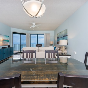 Dining area with a dark wood table, overlooking a cozy living space with a sofa and stunning views of the gulf