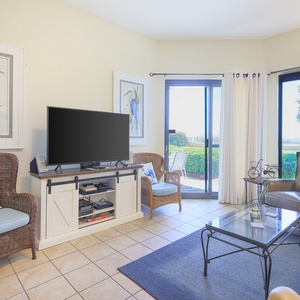 The inviting living room features a large TV, comfortable seating, and sliding glass doors leading to a serene outdoor patio