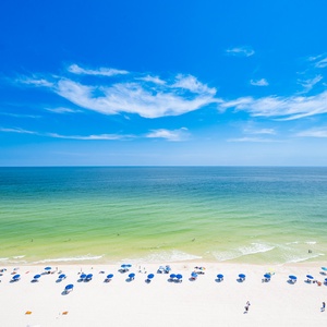 Breathtaking view of the turquoise waters and white pristine beach, dotted with colorful umbrellas under a clear blue sky