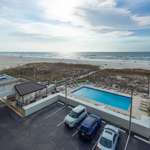 Enjoy stunning beachfront views from this inviting balcony overlooking a sparkling pool and sandy shore