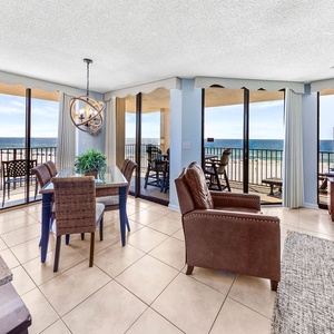 Bright dining area with a glass table, stylish chairs, and a view of the beach through expansive sliding glass doors