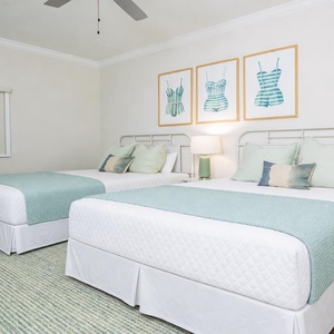 Unwind in the guest room featuring two queen beds with cozy linens, decorative pillows, and a relaxing vibe