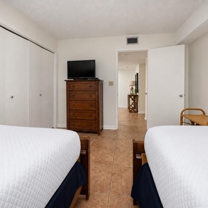 Guest bedroom featuring two double beds, a TV, and a charming view into the hallway with decorative accents