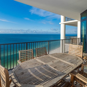The spacious balcony features a wooden dining set with stunning views of the beach, perfect for outdoor meals and relaxation