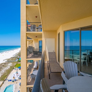 Expansive view of a serene beach with white sand, dotted with blue umbrellas and sunbathers, inviting relaxation and fun