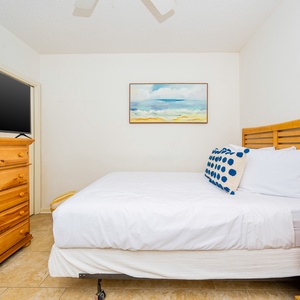 Relax in this comfortable guest bedroom featuring a queen bed, a TV, and a charming beach-themed painting on the wall