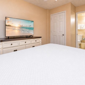 This bedroom features a comfortable king bed, a large TV for entertainment, and soft beige tones for a calming atmosphere
