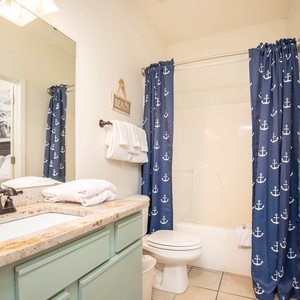 The bathroom features a light blue vanity with a stylish countertop, a tub/shower combo, and nautical shower curtains