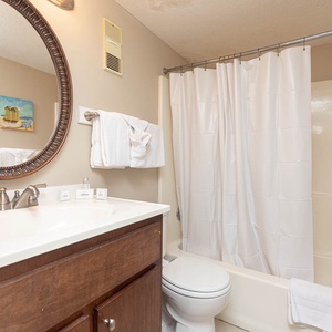 This bathroom features a stylish round mirror, a clean white shower curtain, and fresh towels, creating a refreshing space