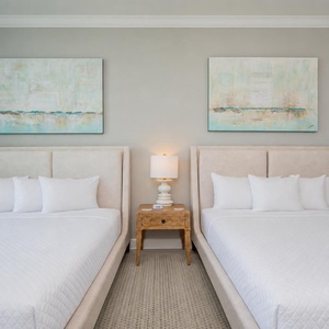 Serene guest bedroom featuring two plush queen beds, soft lighting, and calming artwork
