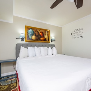 The bedroom features a large king bed with multiple pillows, decorative wall art, and soft lighting from wall sconces