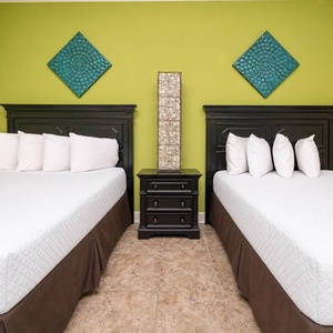 This vibrant guest bedroom features two queen beds with plush pillows and a stylish green accent wall, perfect for relaxation
